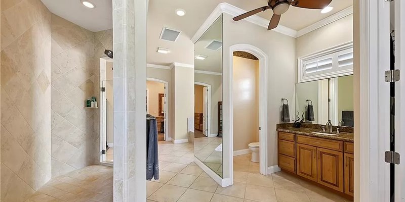 Elegant bathroom featuring a spacious walk-in shower, double vanity with granite countertops, large mirrors, and a ceiling fan.