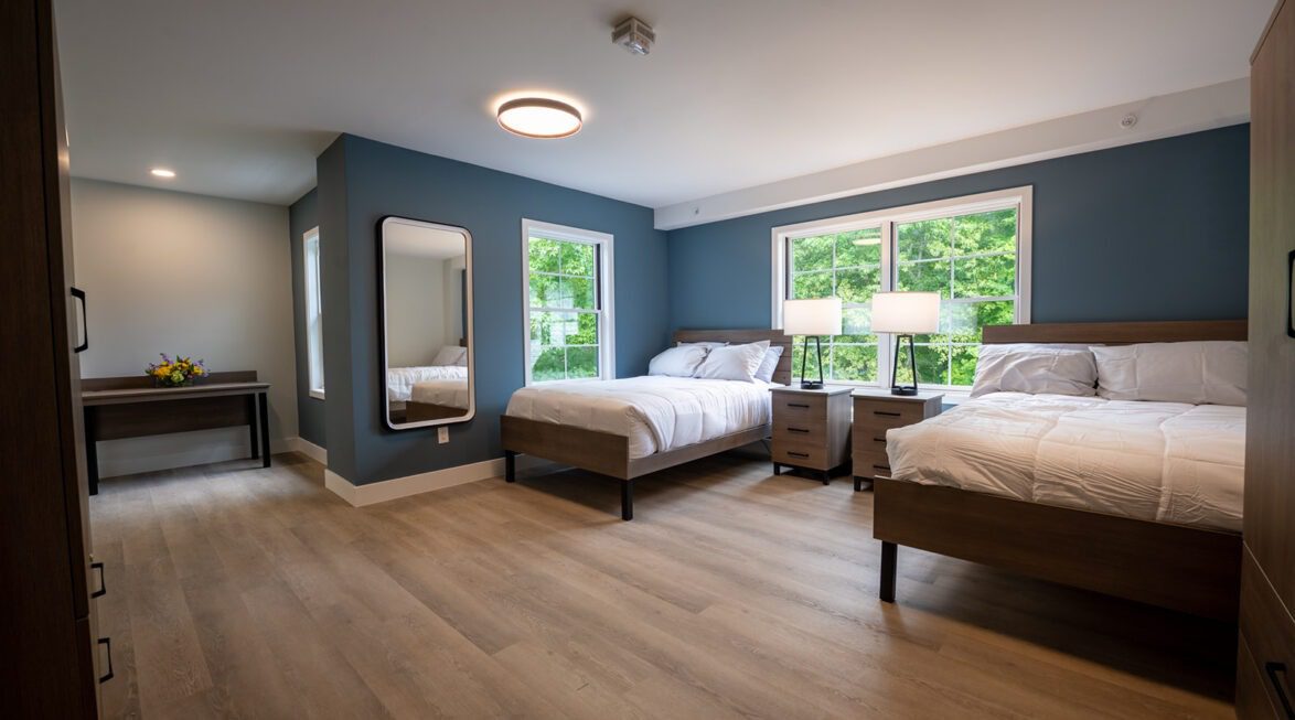Spacious shared bedroom with two full-size beds, nightstands, and large windows