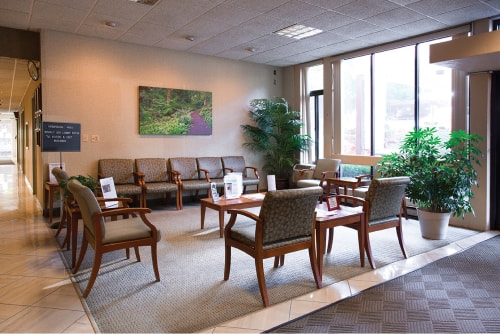 A spacious waiting room with chairs, tables, and large windows.