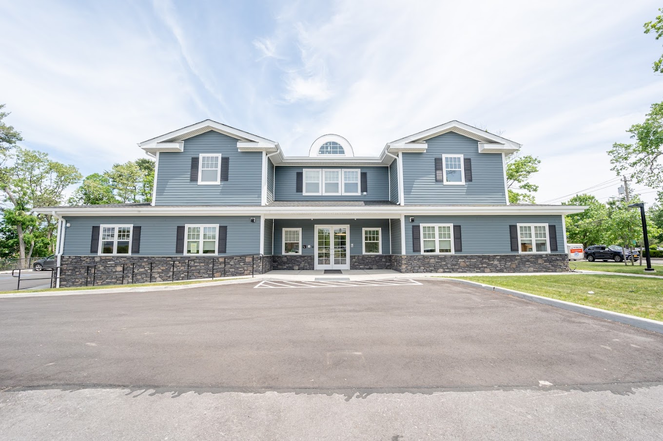  A two-story building with blue siding and stone accents, featuring a clean and welcoming entrance with large windows and an accessible driveway.