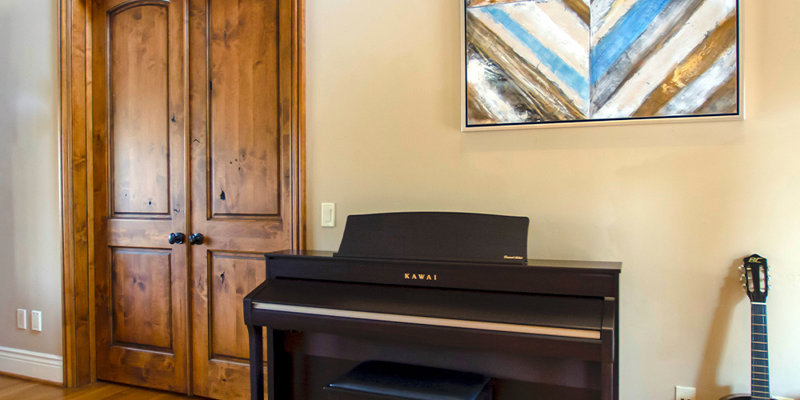 A warm, inviting room featuring a piano, a guitar, wooden double doors, and artistic wall decor, creating a peaceful and creative atmosphere.