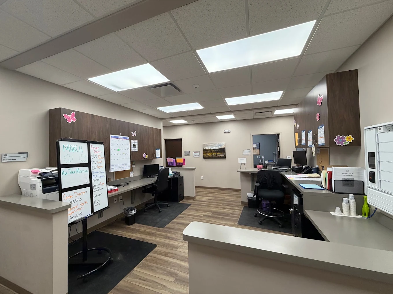 BrightView Health clinical workstation with desks, computers, storage cabinets, whiteboard, printer, and wood-look flooring