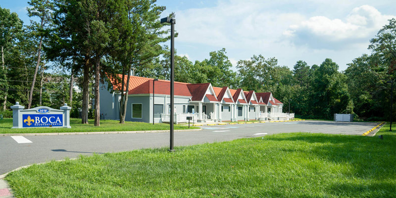 A serene exterior view of Boca Recovery Center, featuring charming buildings with red roofs, surrounded by greenery and ample parking space.