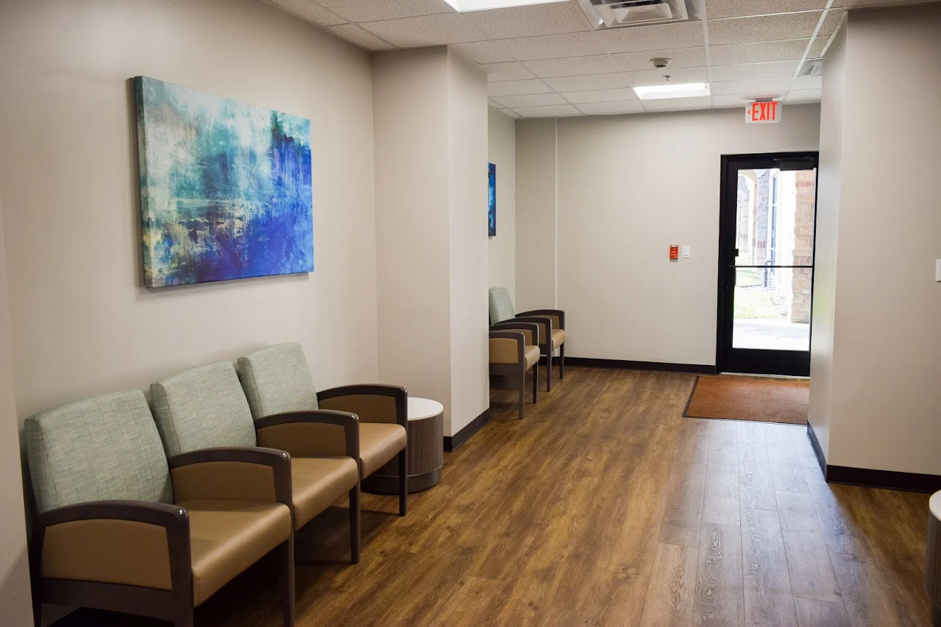 Padded chairs in hallway with artwork and wood flooring