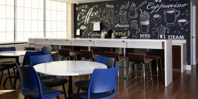 A cozy café-style space features vibrant seating, a chalkboard menu wall, and a coffee bar, offering a welcoming spot for relaxation and socializing.