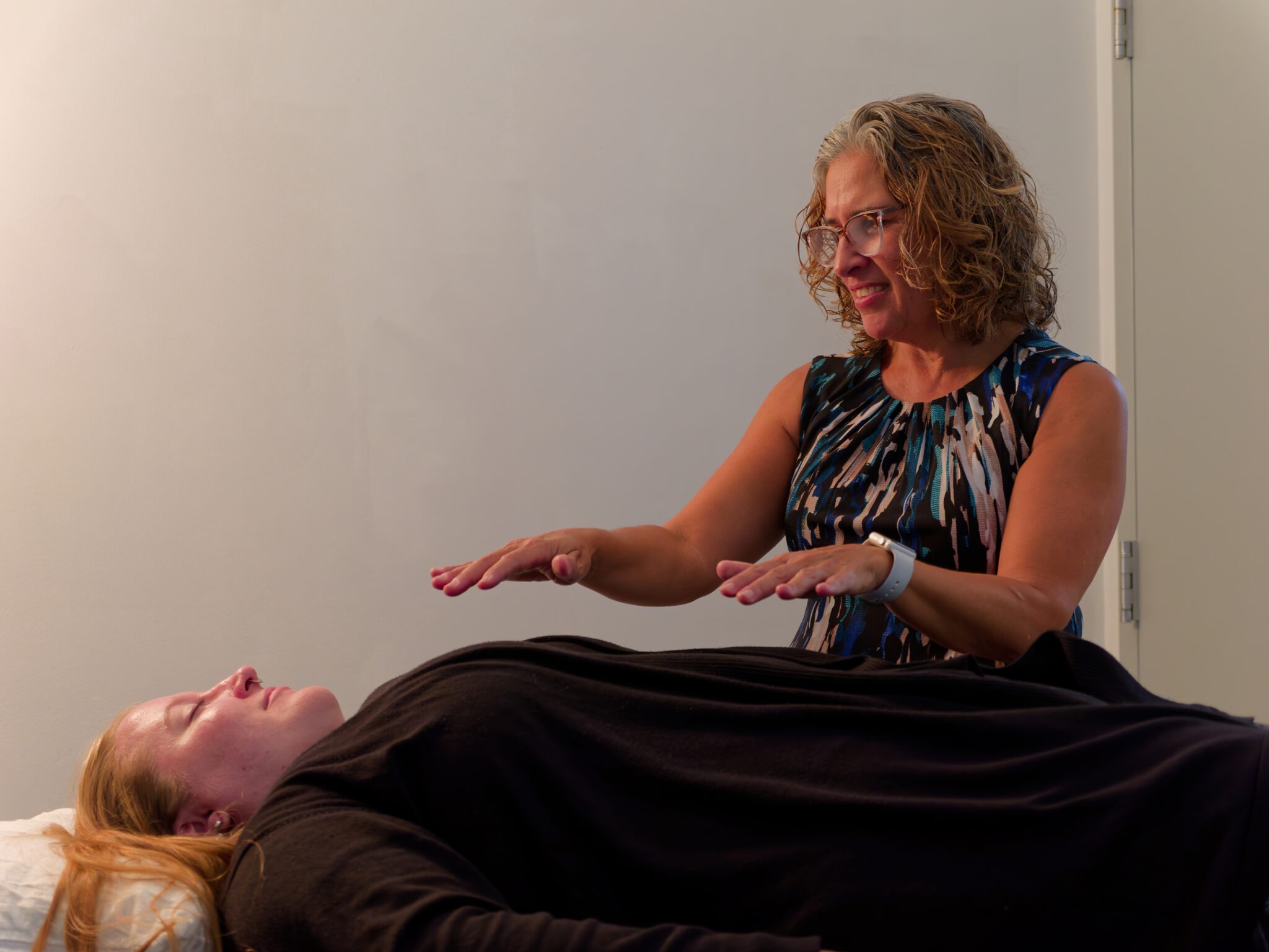 Practitioner providing reiki to a client lying on a treatment table.