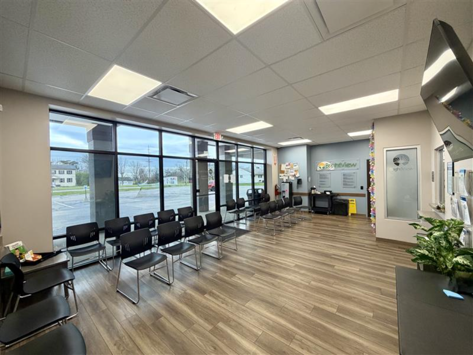 Spacious BrightView Health Middletown lobby with rows of black chairs, large front windows, reception area, and wood-look flooring