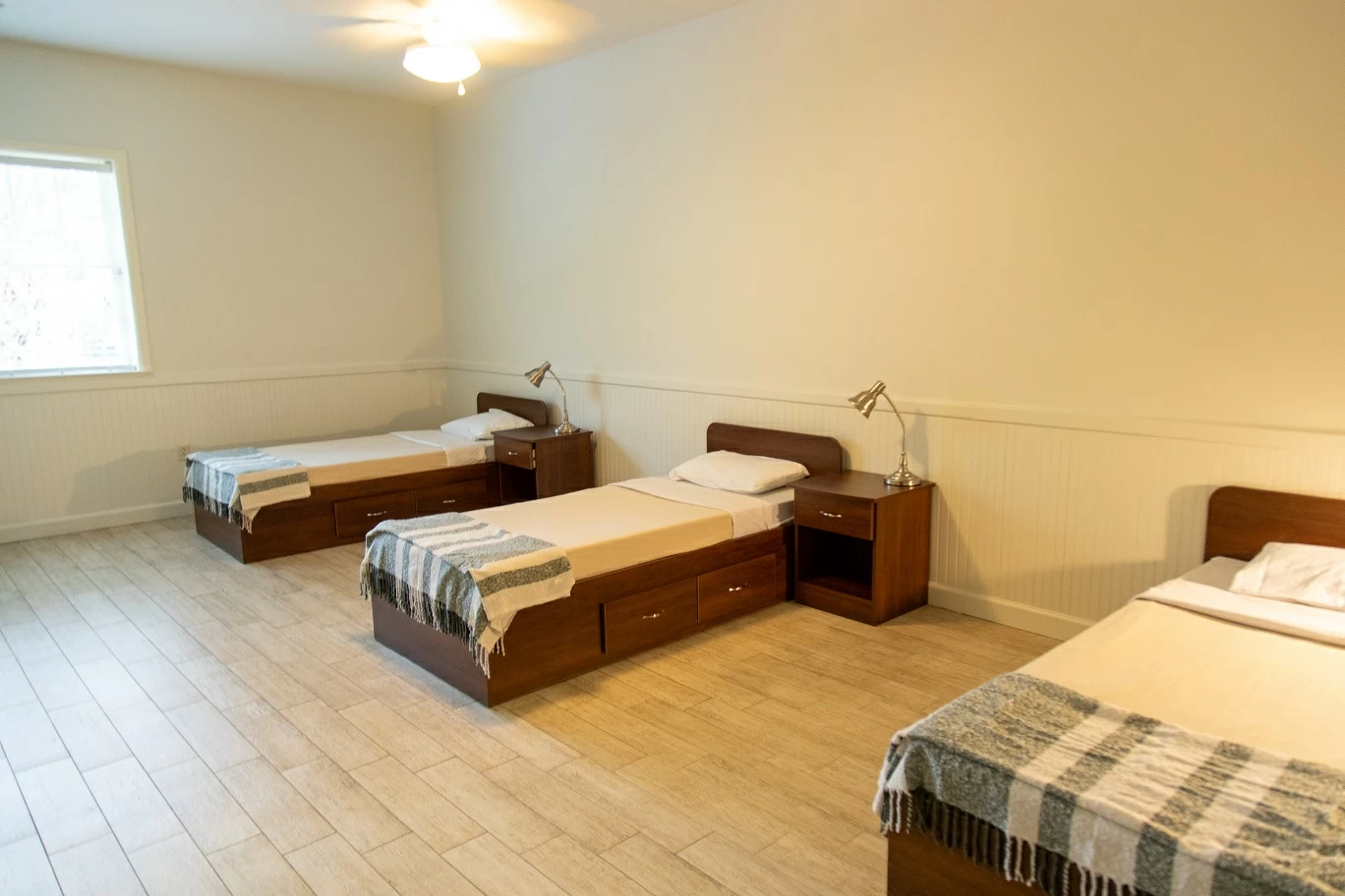 Bedroom with three single beds, bedside tables, and neutral decor inside residential treatment facility
