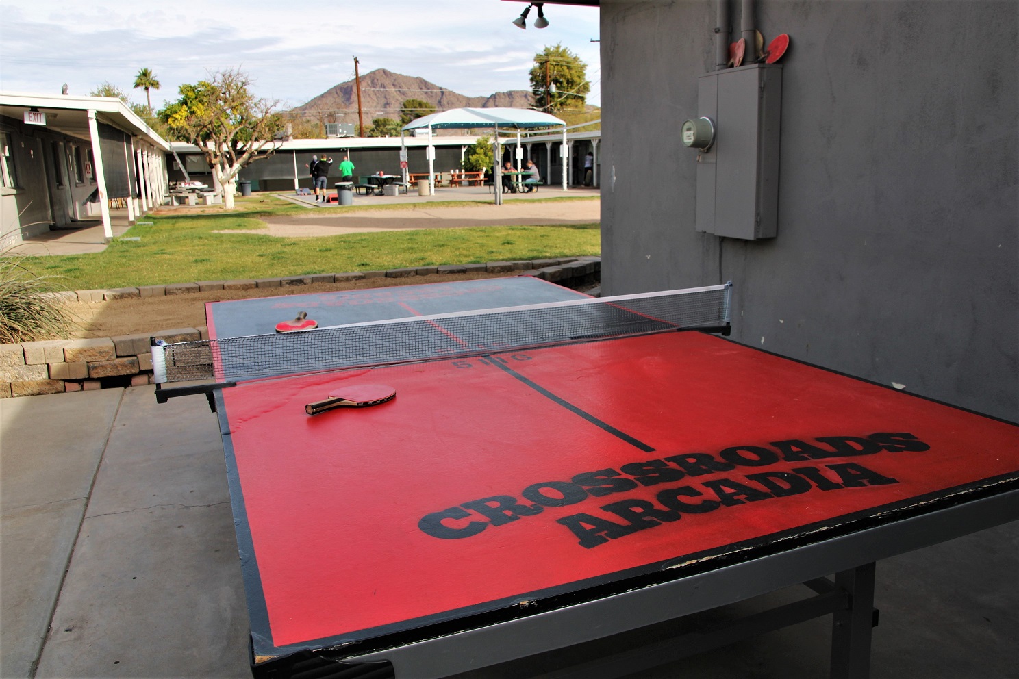 Red outdoor ping pong table labeled "Crossroads Arcadia" with mountain in background