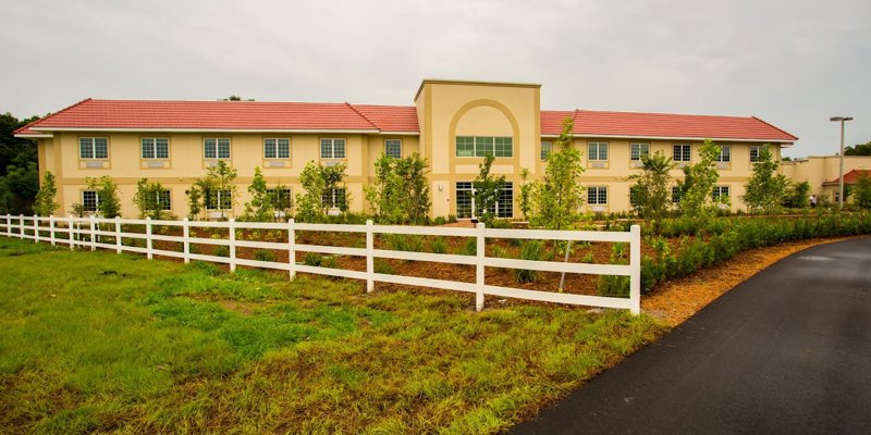 A welcoming two-story building with a red roof, surrounded by lush greenery and a white fence, creating a serene and inviting atmosphere.