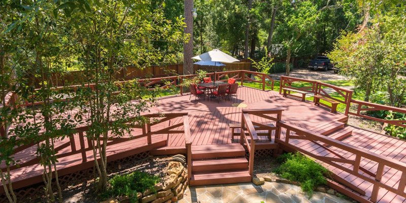 A spacious wooden deck surrounded by trees offers a peaceful outdoor seating area with a table, chairs, and an umbrella, perfect for relaxation.