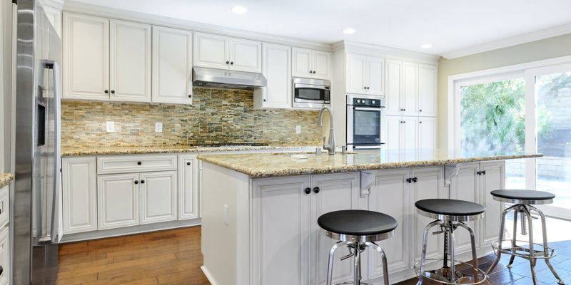 A bright, modern kitchen featuring white cabinets, granite countertops, a stainless steel fridge, and an island with barstools, offering ample space.