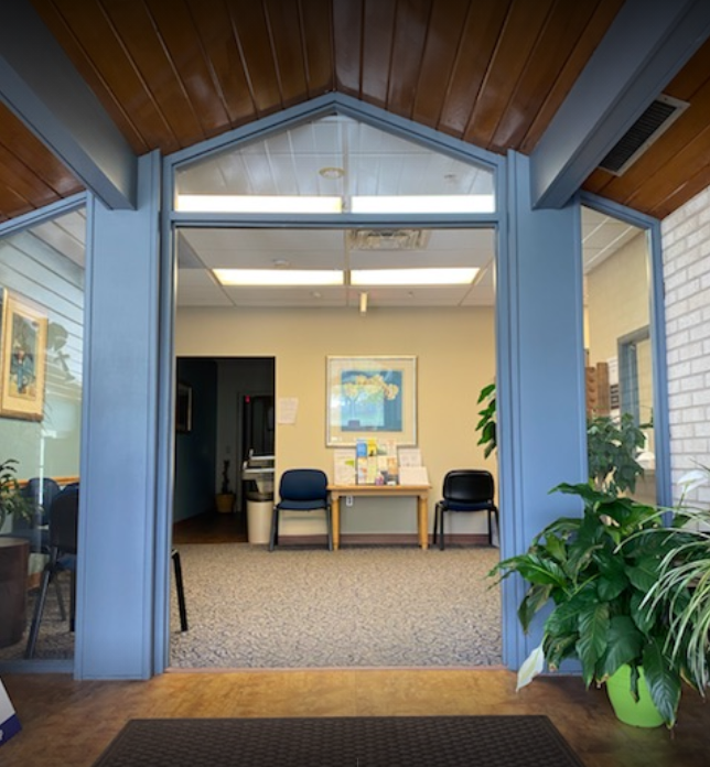 Glass entryway leading to waiting area with chairs and indoor plants