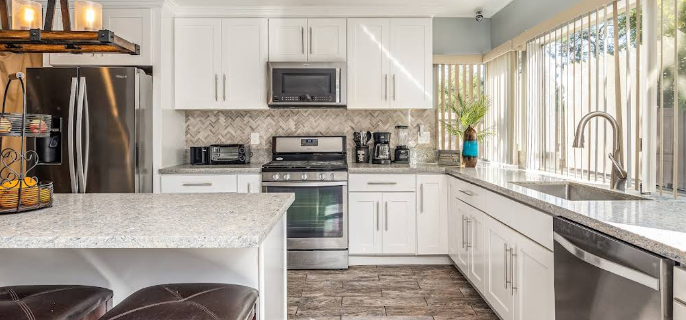 Bright kitchen with white cabinets, stainless appliances, and long windows.