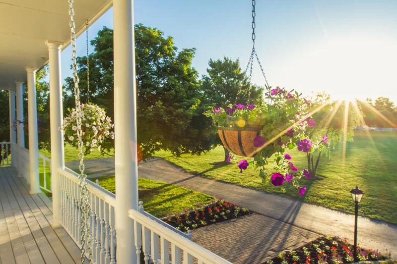 View from the porch featuring hanging flower baskets, sunrise light, and landscaped paths surrounded by green lawns