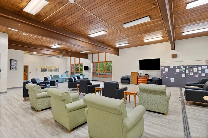 Spacious common area with multiple seating arrangements, wood-paneled ceiling, and large windows.