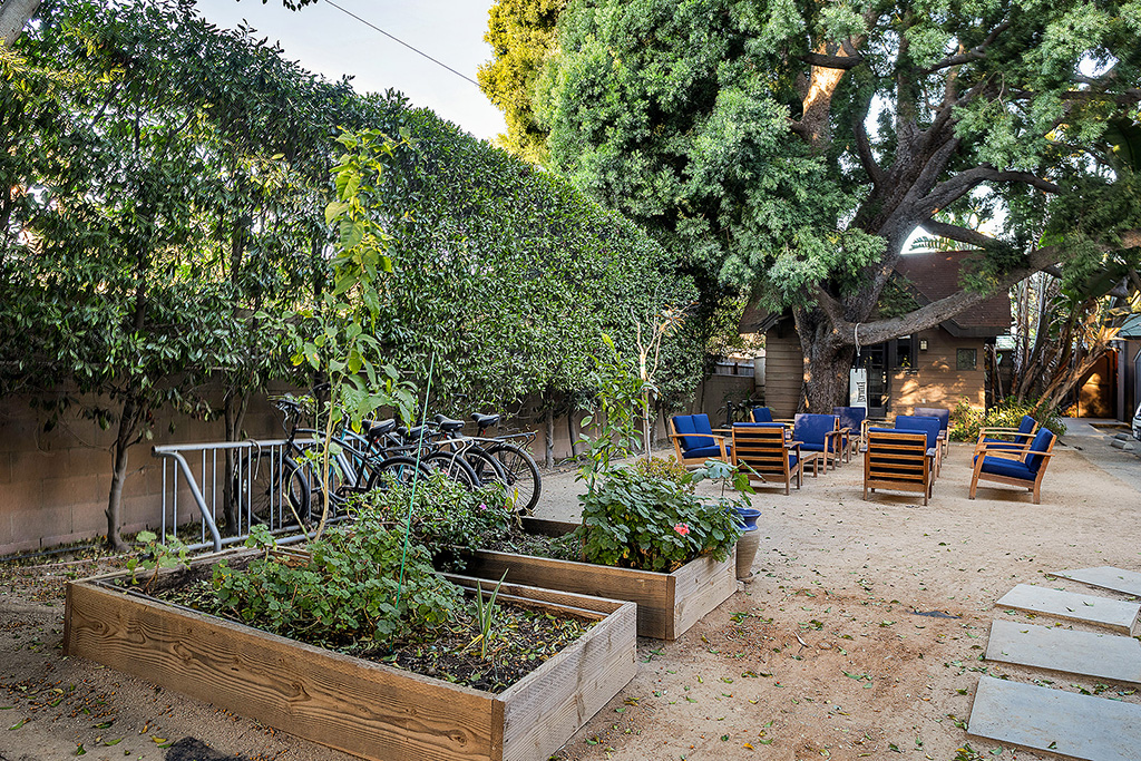 Outdoor garden with planter boxes, blue chairs, and shaded trees