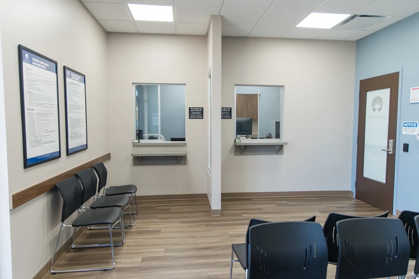 Patient service area with two service windows, seating, informational posters, and a BrightView-branded door