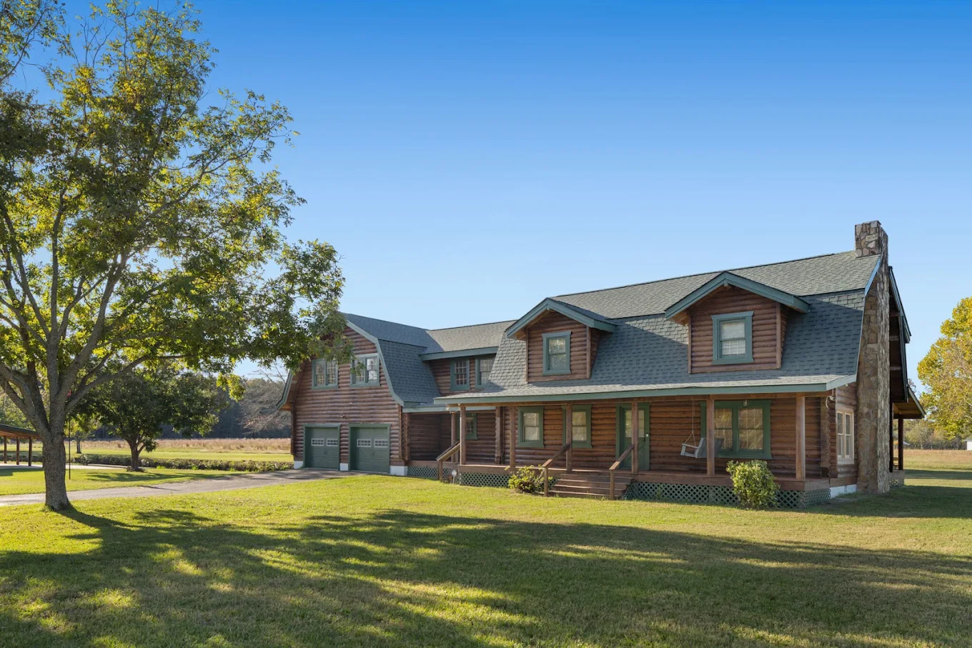 Large log cabin facility with covered porch, garage, and lawn