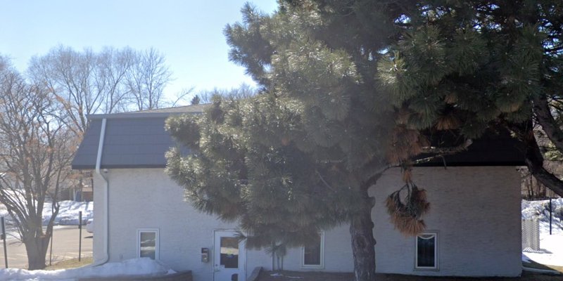 A peaceful building surrounded by nature, featuring large trees and a bright, sunny sky, creating a serene and welcoming atmosphere.