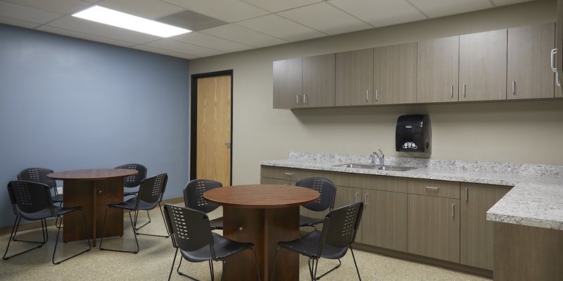 A clean, organized break room featuring round tables, comfortable chairs, and a modern kitchenette, offering a welcoming space for relaxation.