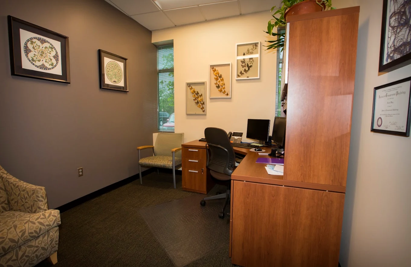 Private counseling office with a desk, computer, guest seating, framed artwork, and wood cabinetry