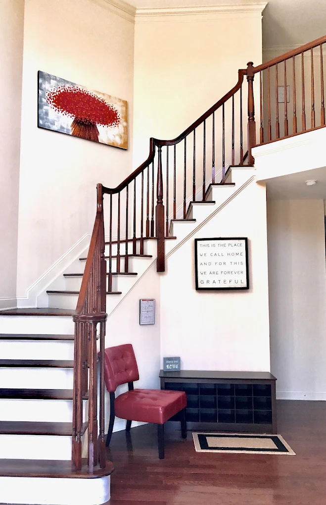 Bright entryway with wooden staircase and red accent chairs.