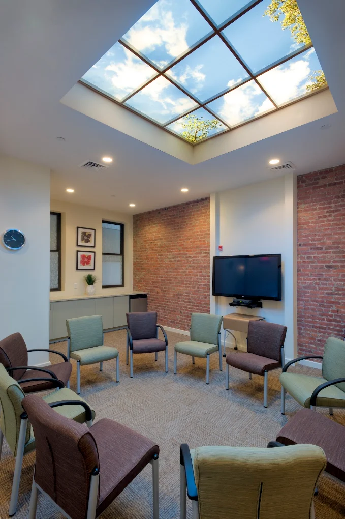 Group meeting room with chairs arranged in a circle, exposed brick walls, television, and large skylight