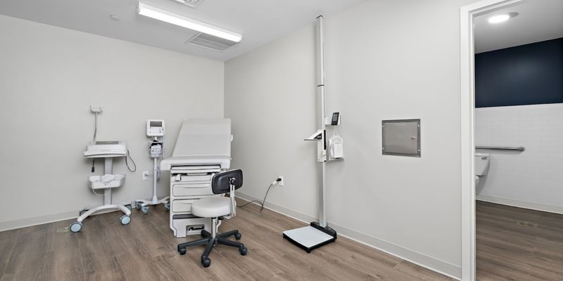  A clean and modern medical examination room with an exam table, medical equipment, and wooden flooring. The room feels professional and welcoming.