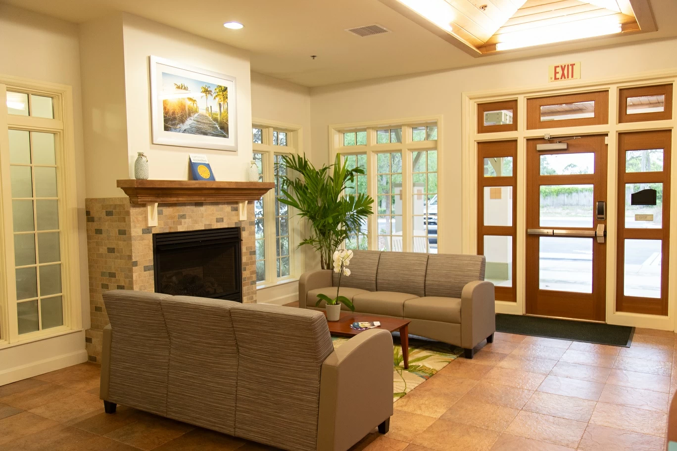 Comfortable lounge area with sofas, fireplace, large windows, and entrance doors at treatment center