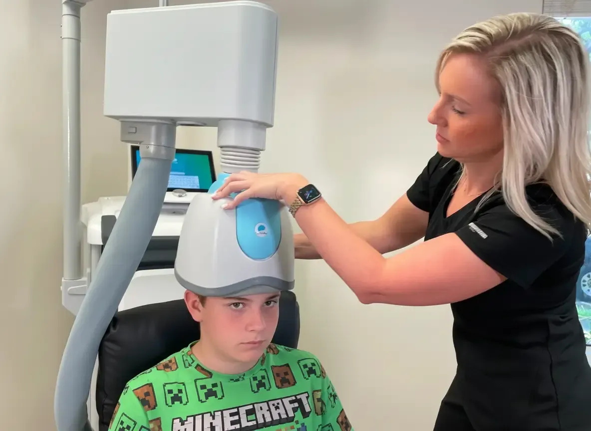 A medical professional administering TMS therapy to a teen boy.