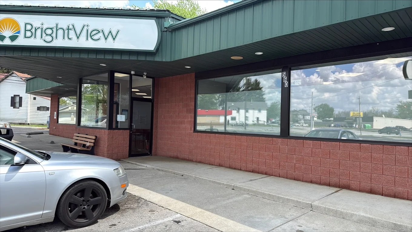 Front exterior of BrightView Health Marion with large BrightView sign, green metal awning, red block facade, glass entrance and windows, bench, and parking area