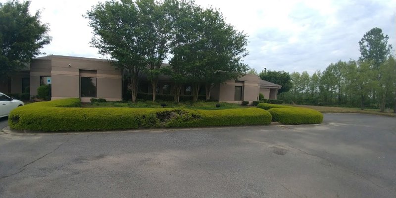  A single-story building with large windows and neatly trimmed hedges, surrounded by trees and greenery, creating a peaceful and private atmosphere.