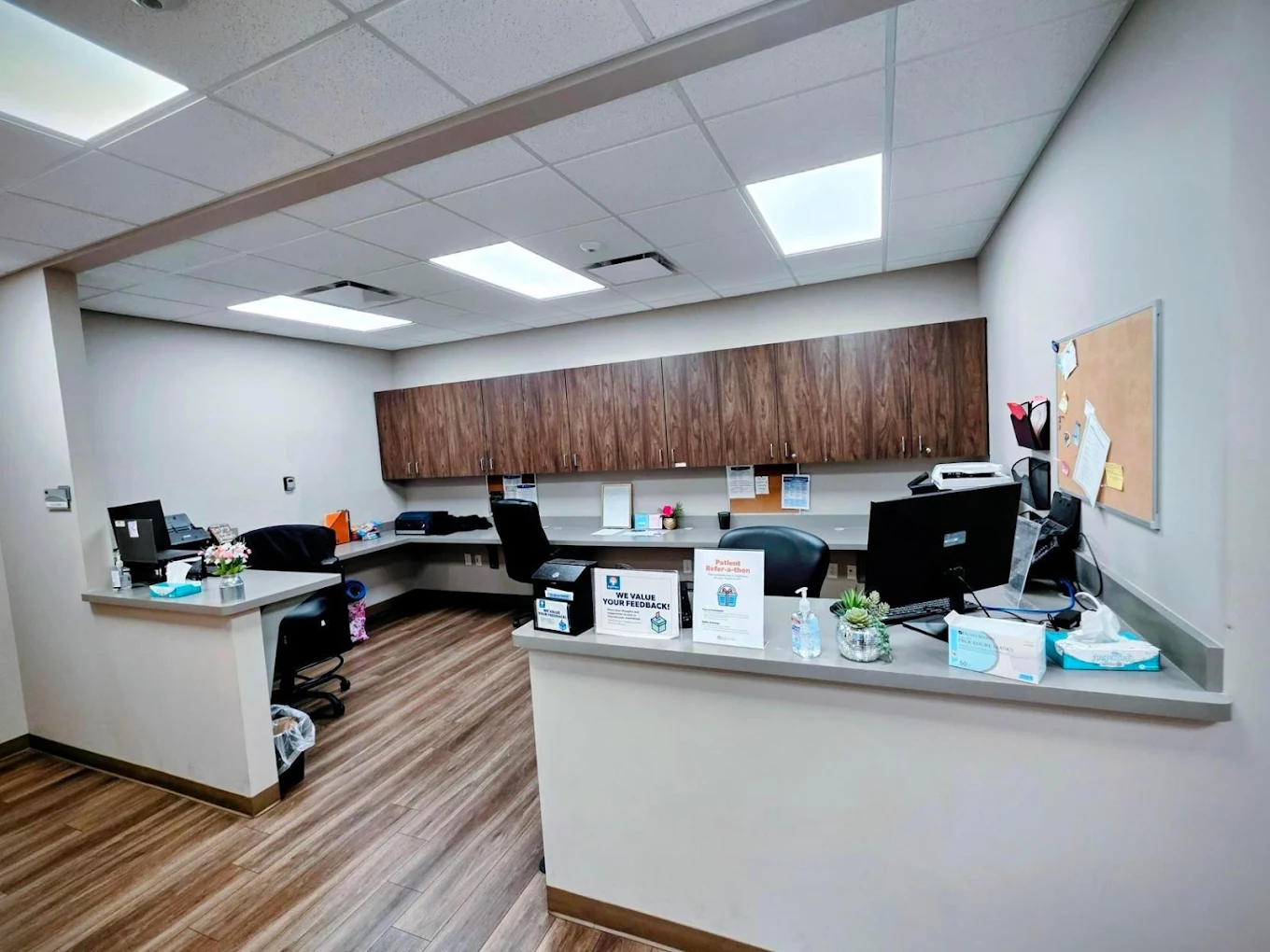 BrightView Health reception and staff workstation with front counter, computers, overhead cabinets, office chairs, and wood-look flooring