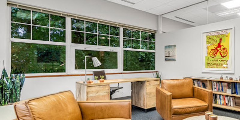 Cozy seating area with leather chairs and a round coffee table in a well-lit room. Large windows offer a peaceful view of nature.