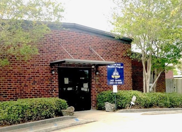 Brick facility entrance with trees and landscaped shrubs