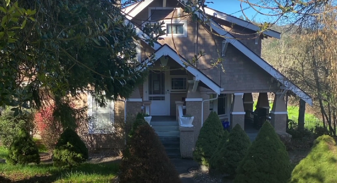 Front view of main house with porch and landscaped shrubs