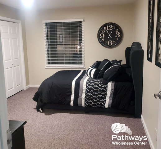 Stylish bedroom with a neatly made bed in black and white bedding, wall clock, and large window at Pathways Wholeness Center