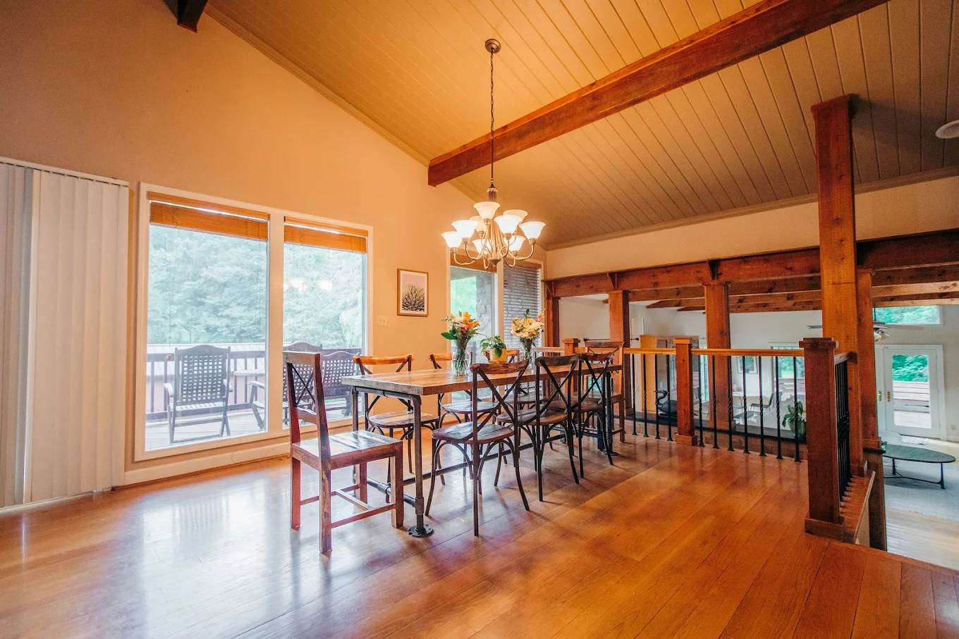 Wooden dining table with chairs under a chandelier near large windows and balcony access
