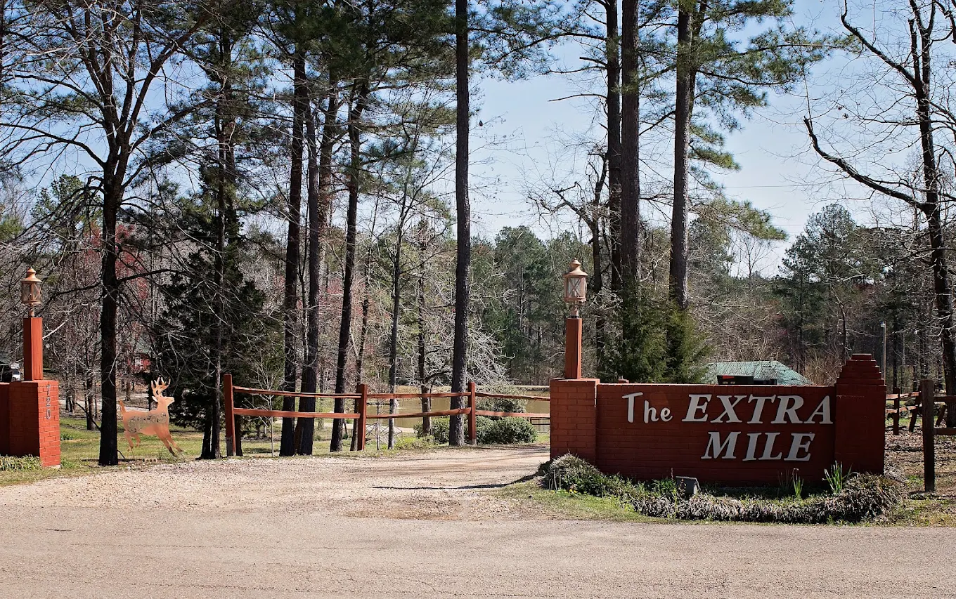 Extra Mile entrance sign along a wooded driveway