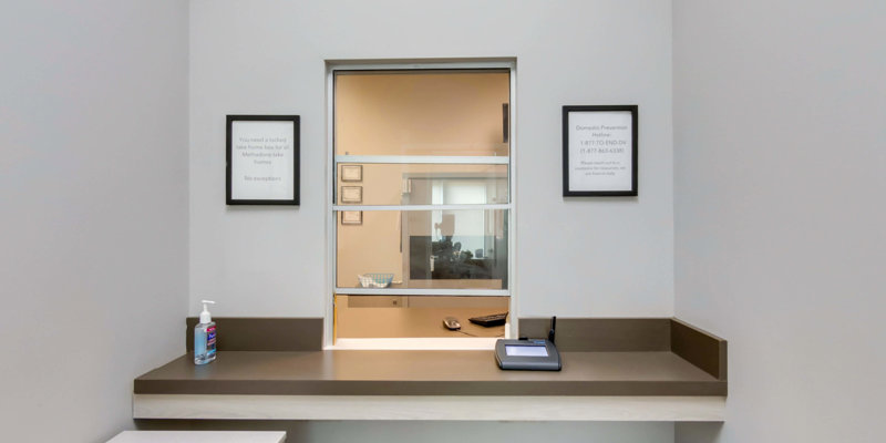 A clean reception window with informational signs on the wall and a hand sanitizer bottle on the counter, creating a professional and orderly check-in area.