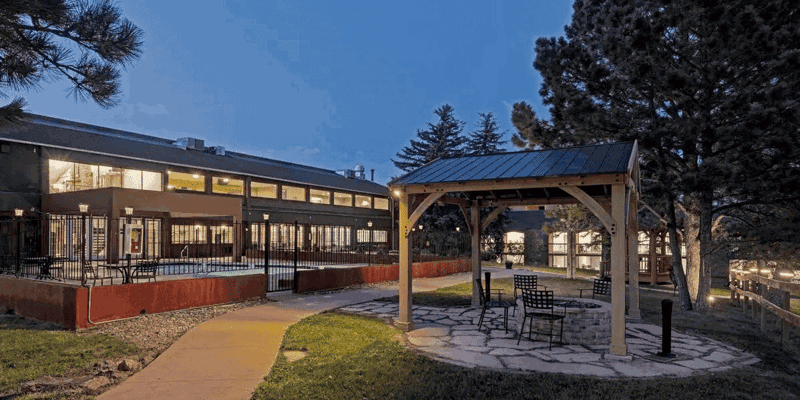 Peaceful outdoor setting with a cozy gazebo, fire pit, and comfortable seating, surrounded by trees and soft evening lighting for relaxation.