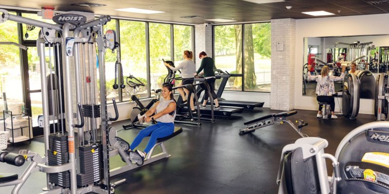 Modern fitness center with large windows, natural light, and various exercise equipment.