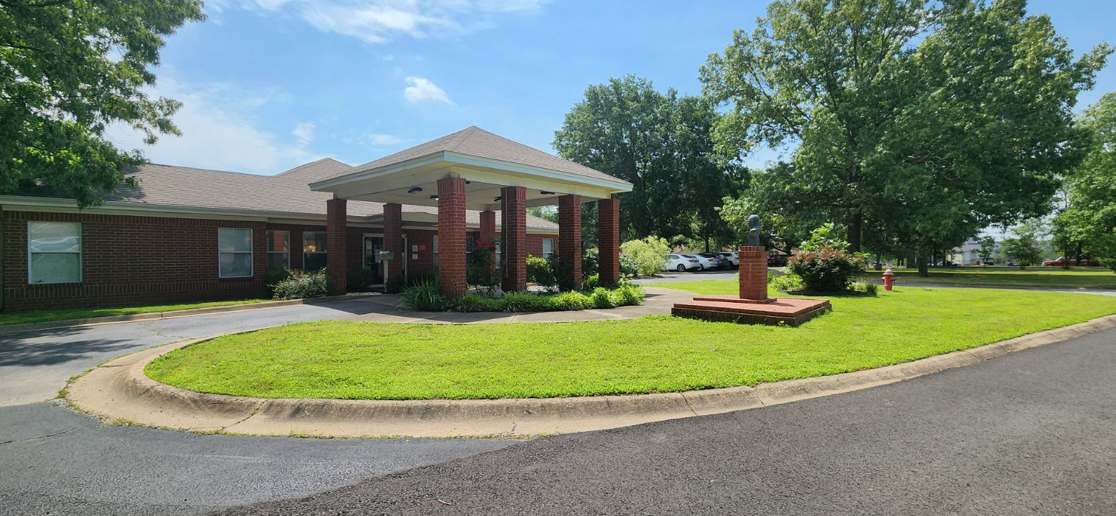 Brick facility with covered entrance surrounded by lawns and trees