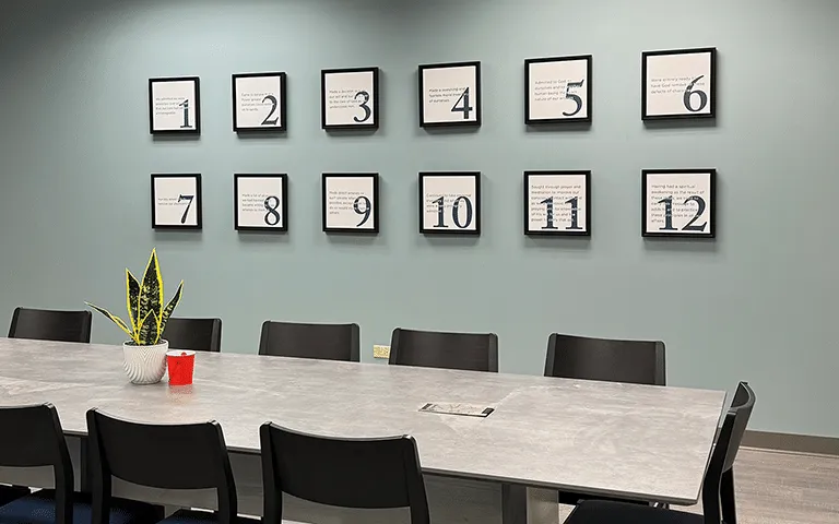 Meeting table and chairs beneath a Twelve Steps wall display