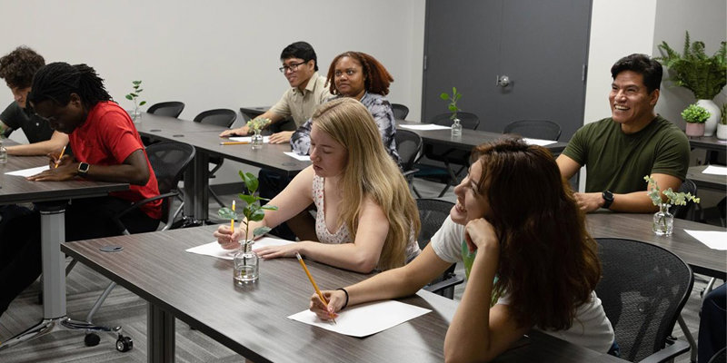  A group of engaged students participates in a classroom activity, smiling and focused, surrounded by small plants that create a calming atmosphere.