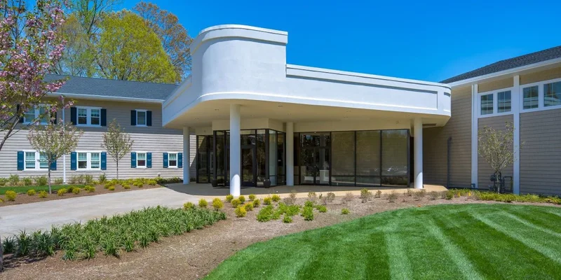 A modern facility entrance with sleek architecture, well-manicured lawns, and blooming trees, offering a welcoming and serene atmosphere.