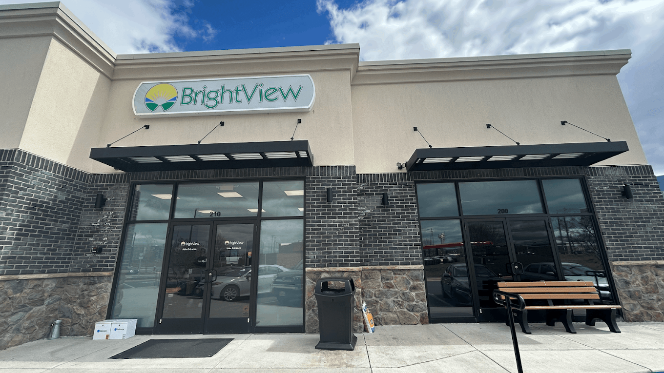 Exterior entrance of BrightView Health Winchester with BrightView signage above glass doors, black awnings, a bench, and stone-and-brick facade