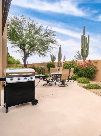 Outdoor patio with barbecue grill, table, chairs, desert landscaping, and tall cacti