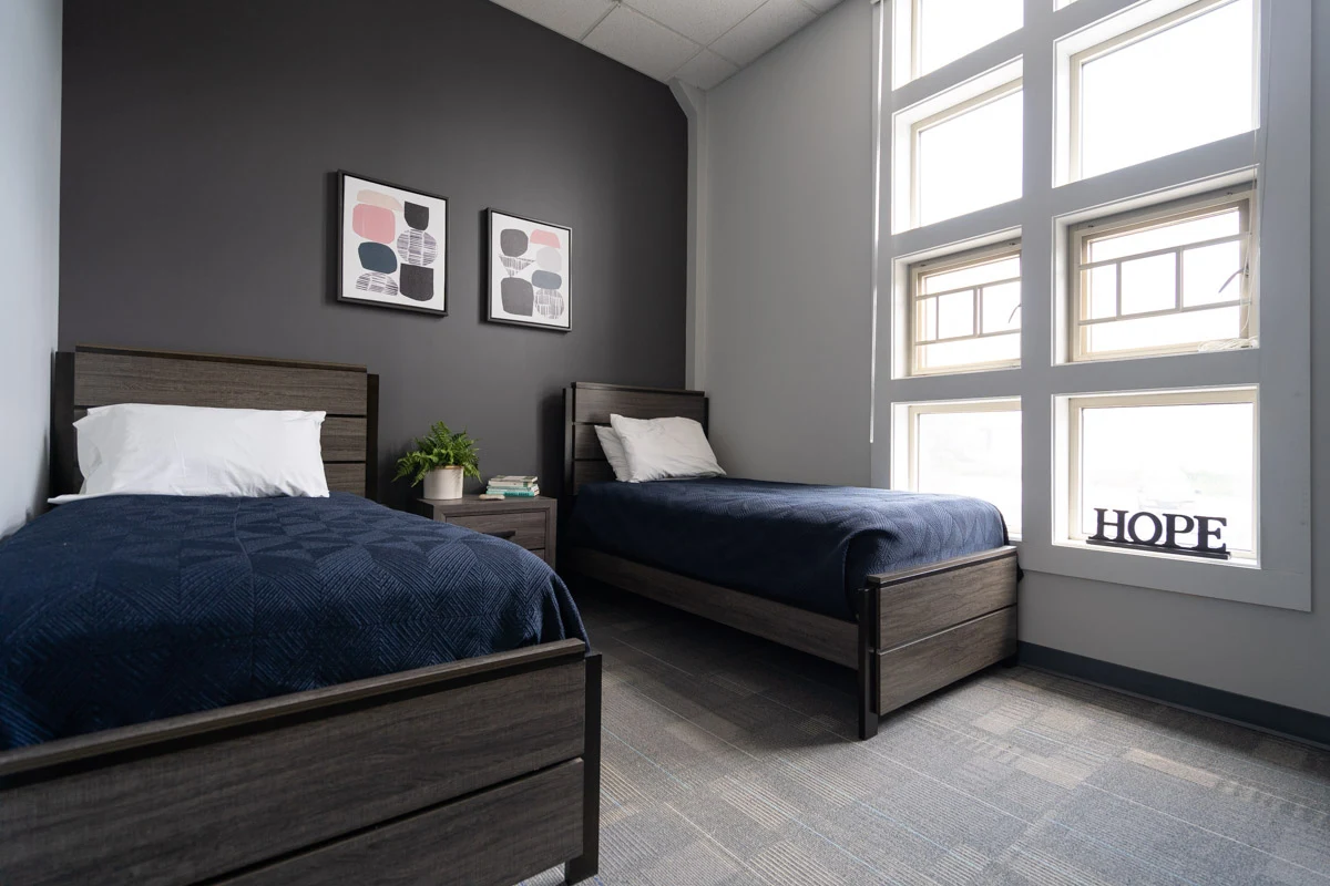 Modern double-occupancy bedroom with twin beds, dark accent wall, large windows, and decorative art pieces